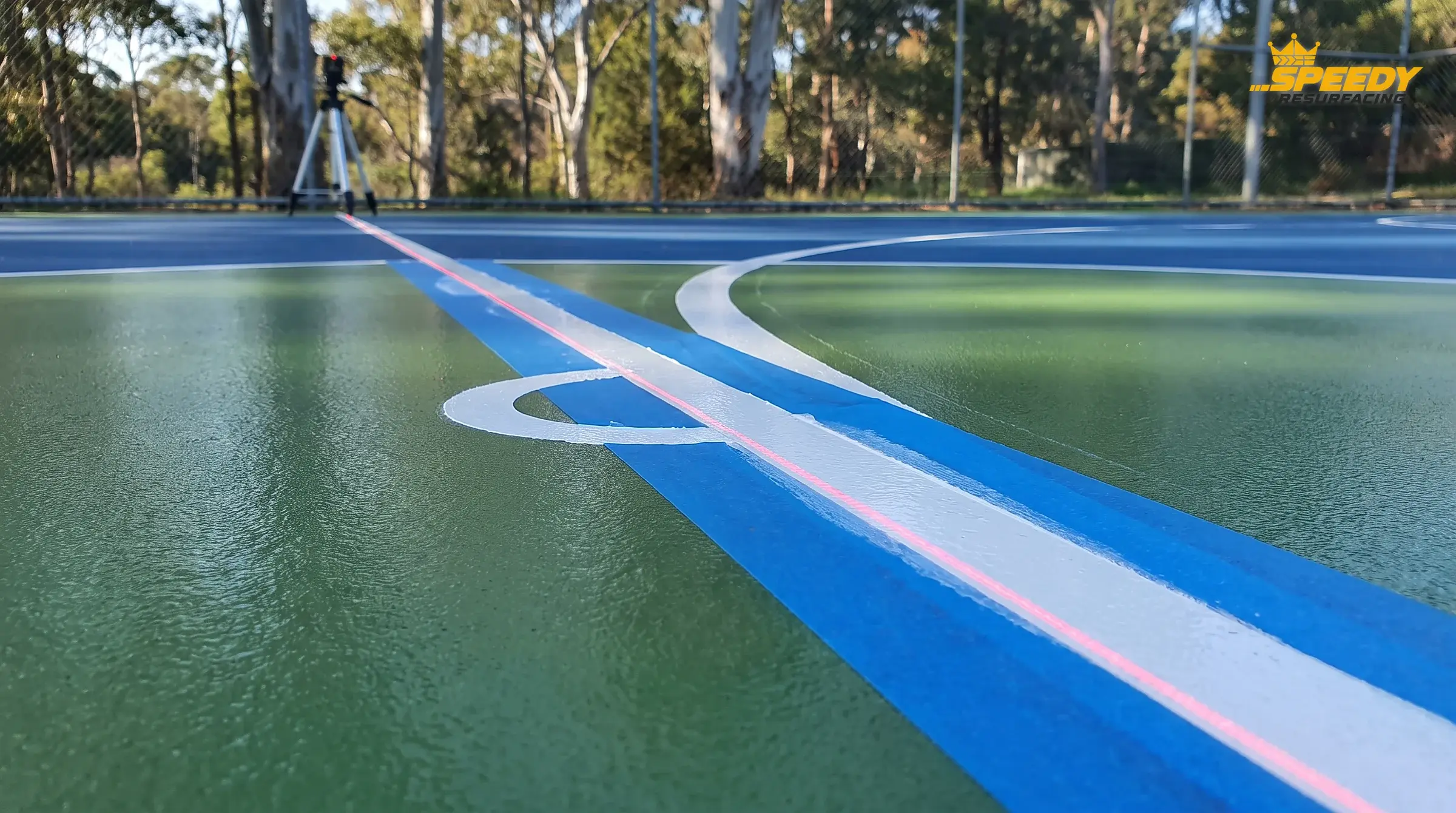 The finish line: laser-guided set-out, sharp-edge masking and regulation boundaries and arcs on the cured two-tone acrylic — the Speedy Line Marking heritage on every court.