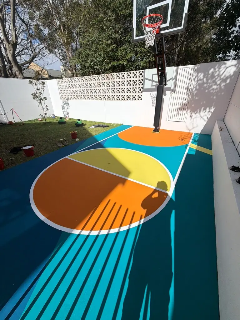 Zones in colour: teal playing surface, navy boundary, split orange-and-yellow centre circle, white regulation lines — poolside in a Sydney backyard.