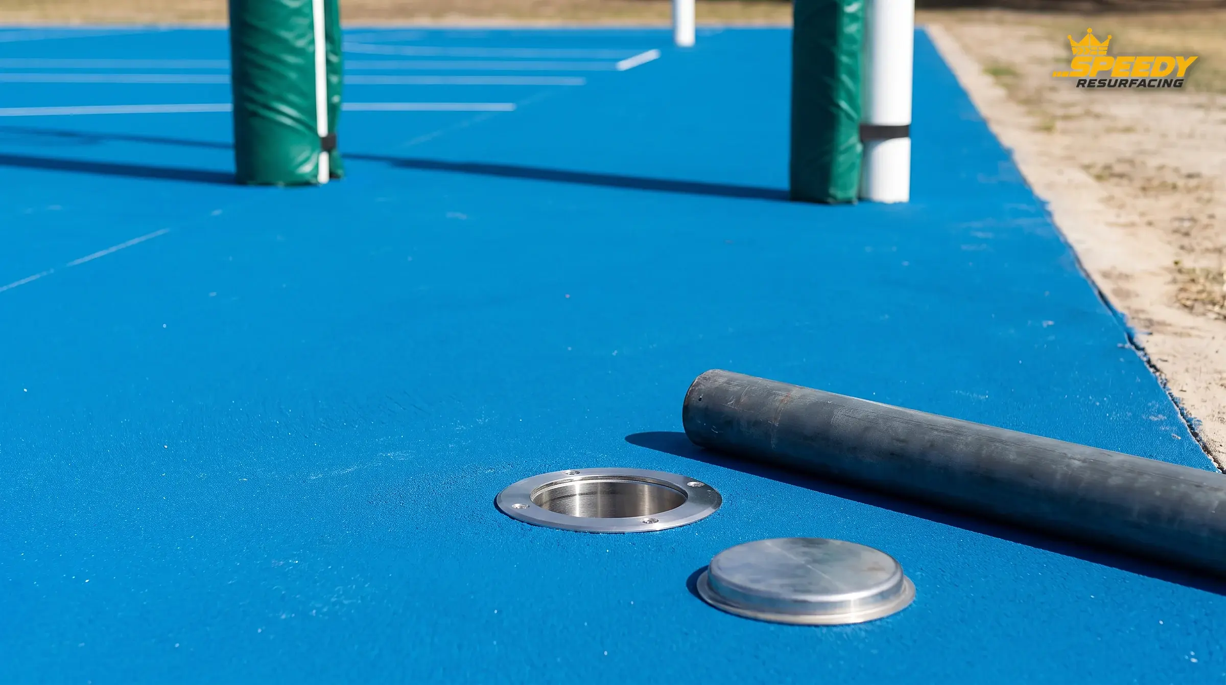 A ground sleeve set flush with the new surface, post lifted out beside it — loose or proud sockets are re-anchored before a drop of acrylic goes down.