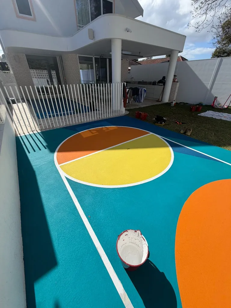 Baseline view of a five-colour backyard basketball court with split orange and yellow centre circle
