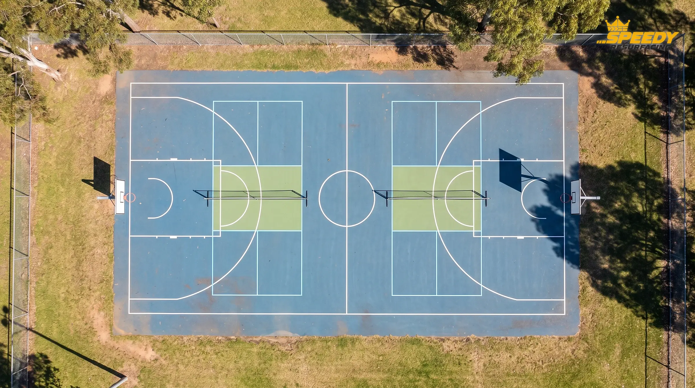 Two pickleball courts laid crosswise on a school basketball court — white basketball lines primary, light-blue pickleball lines secondary, kitchens colour-zoned in green.