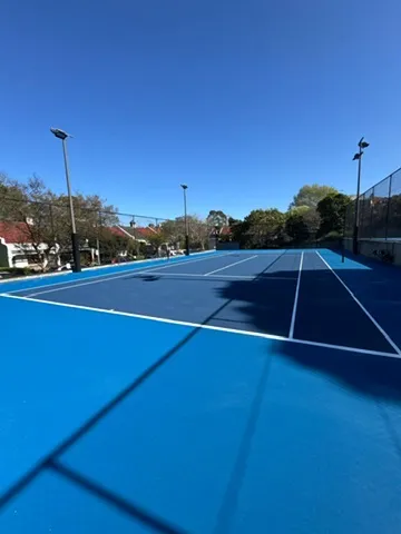Baseline view of a freshly coated blue tennis court under a clear Sydney sky