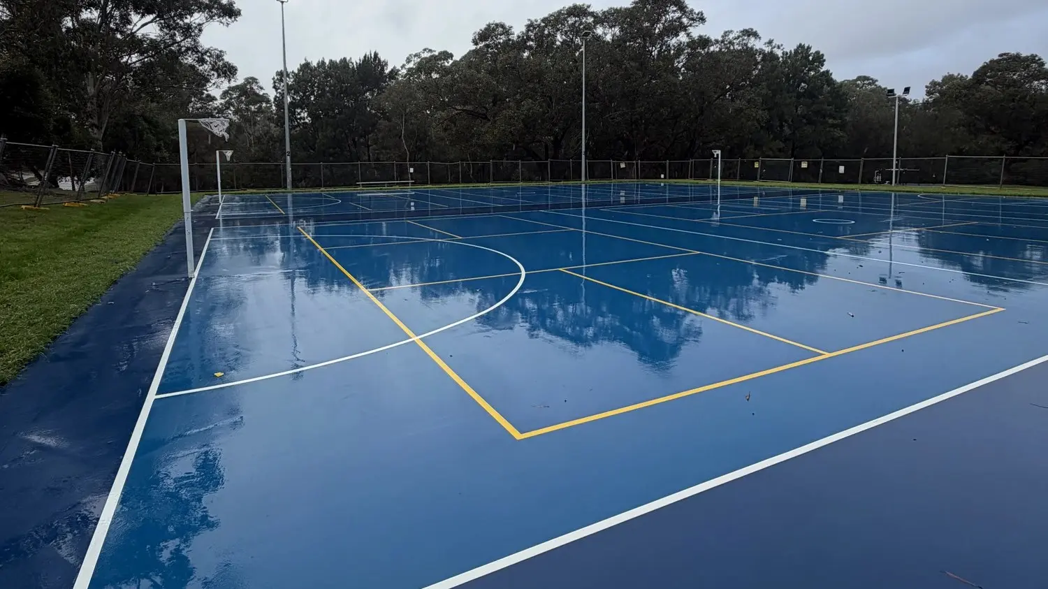 Rain-washed and photo-ready: UV-stabilised two-tone blue acrylic with regulation white netball boundaries — Speedy Resurfacing, Sydney.