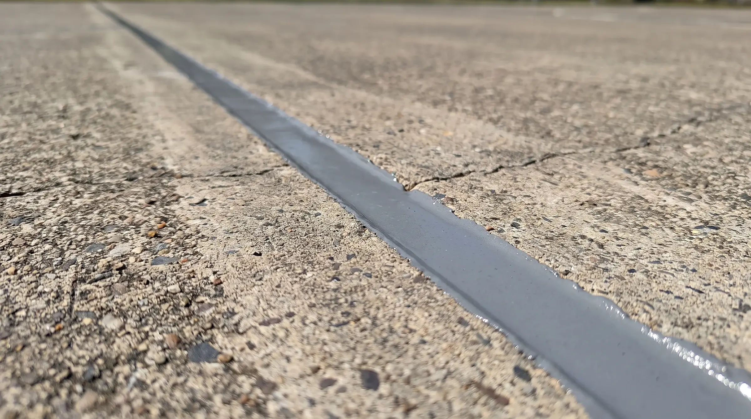 V-routed crack filled flush with flexible polyurea — movement is absorbed in the joint instead of telegraphing through the new surface.